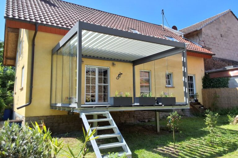 Yellow house with a glass-walled aluminum-framed extension and metal staircase to a raised patio, blue sky above.