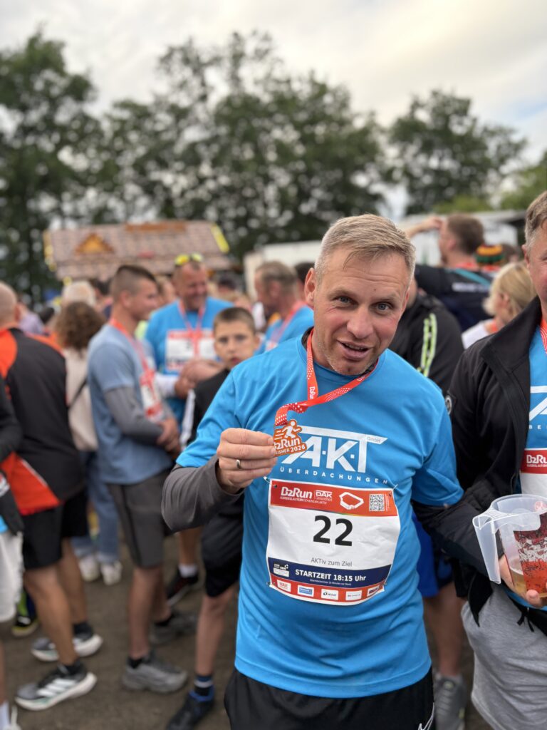 Male runner in a bright blue shirt wearing bib number 22 at a crowded race event, holding an orange medal ribbon toward the camera.